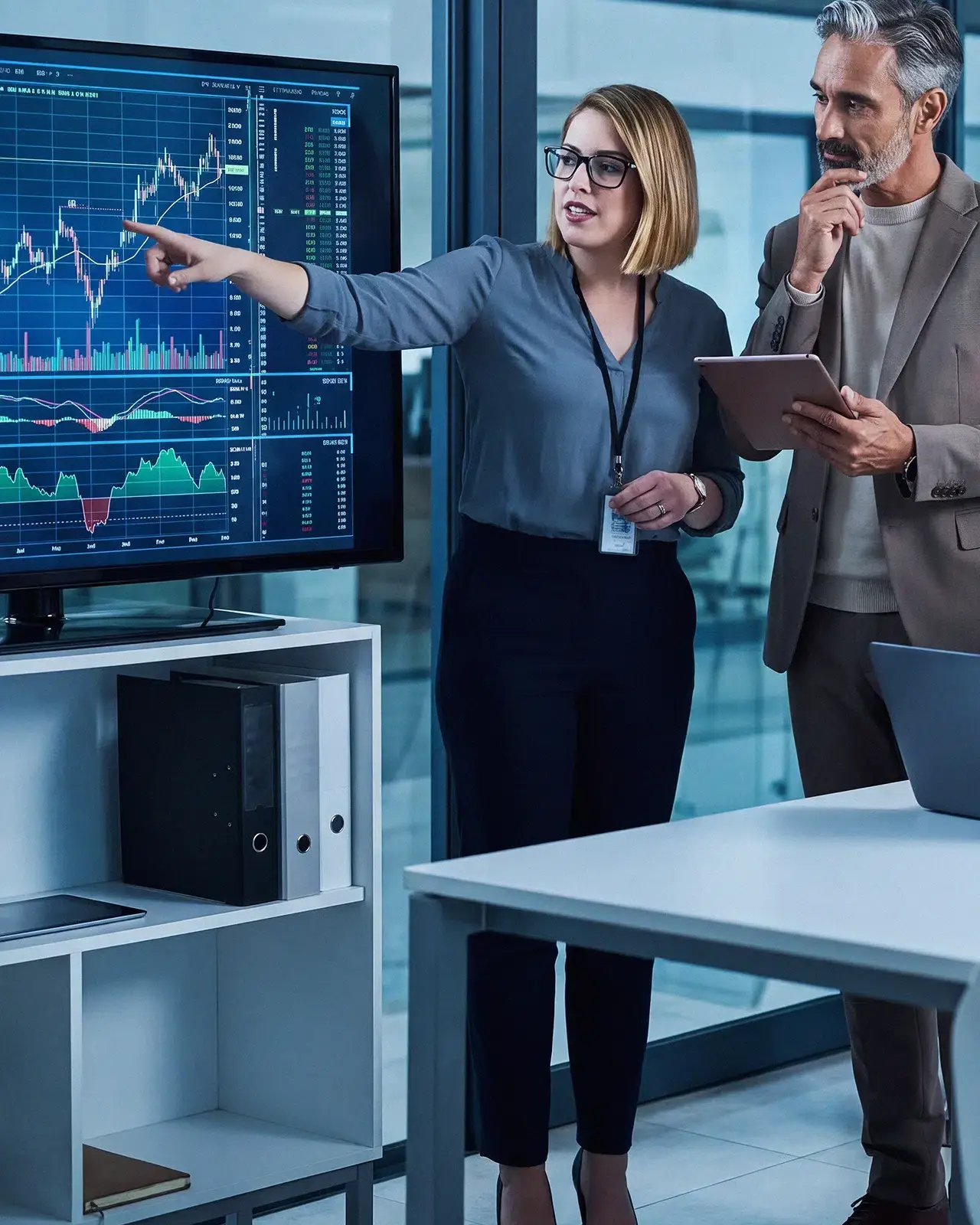 Profissionais analisam gráficos financeiros em monitor de escritório